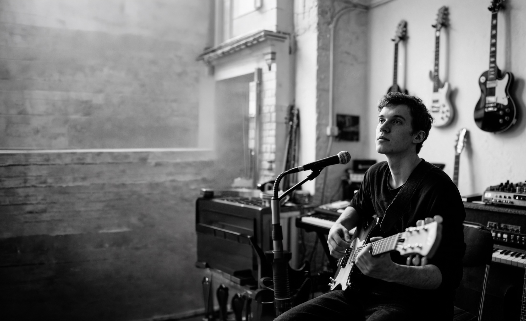 Un musicien guitare en main devant son micro, dans un studio